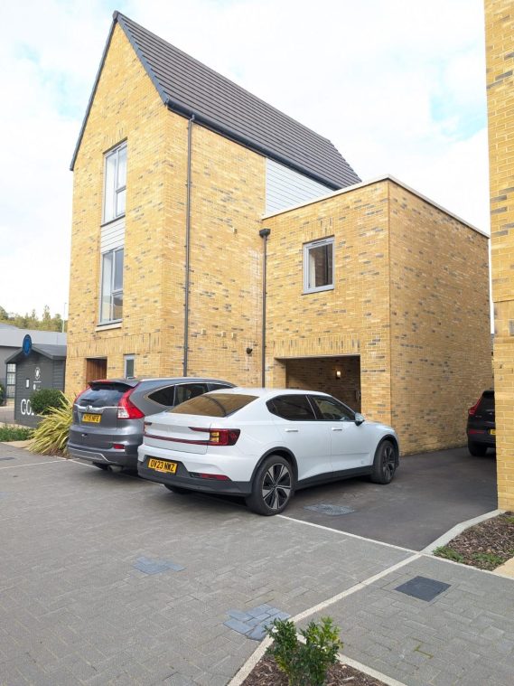 A car parked in front of a house, with two additional cars visible in the driveway.