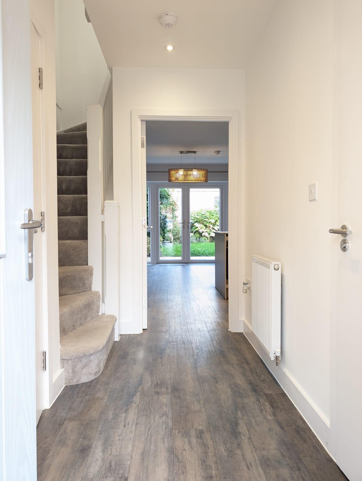 A hallway featuring polished wooden floors and bright white walls, creating a clean and spacious atmosphere.