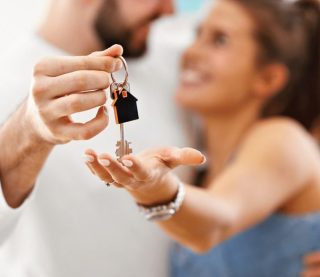 A man and woman joyfully hold keys to a house, symbolizing their new home and shared future together.