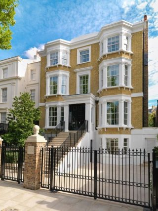 A large white house surrounded by black iron gates, showcasing an elegant and secure entrance.