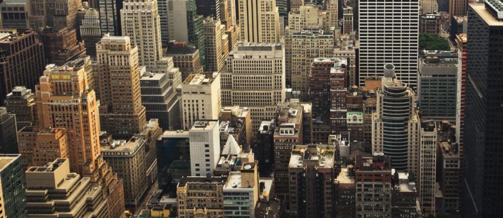  Aerial view of a bustling cityscape, showcasing buildings, streets, and green spaces under a clear blue sky.