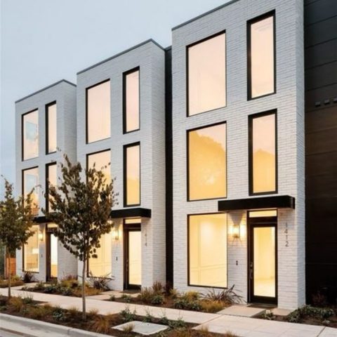 A modern apartment building featuring large windows and a sidewalk in front, showcasing contemporary urban architecture.